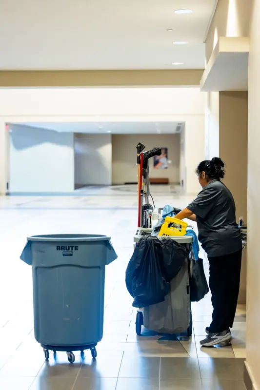 Medewerker met schoonmaakwagen in een lange gang