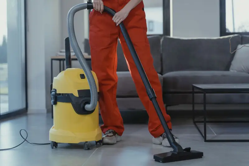 Schoonmaker zuigt een vloer met een gele stofzuiger